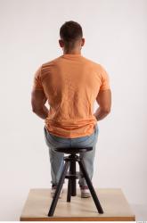 Sitting pose orange thsirt light blue jeans of bodybuilder Harold